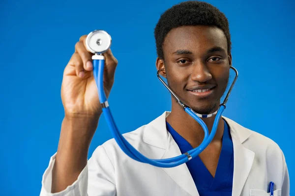 Confiante médico preto posando sobre fundo estúdio azul. — Fotografia de Stock