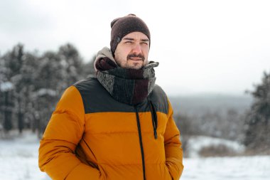 Karlı kış ormanlarında duran kalın paltolu genç adam