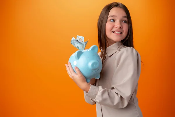 Dospívající dívka s prasátko banka na oranžové barvy pozadí. — Stock fotografie