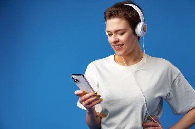 Kulaklıklı genç ve güzel bir kadın mavi arka planda müzik dinliyor.