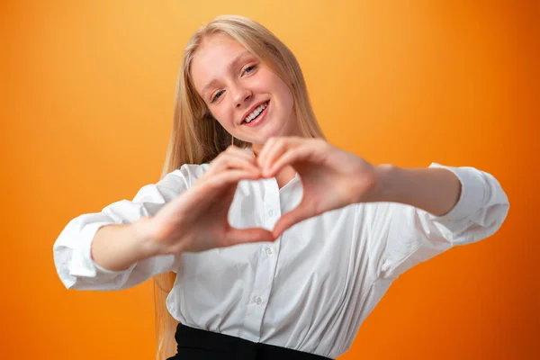 Teen girl showing heart to camera while standing on orange background — Stock Photo, Image