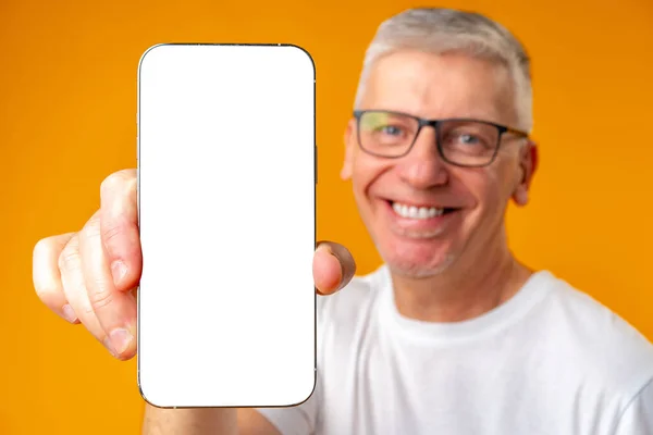 Senior bonito sorridente homem segurando smartphone mostrando tela sobre fundo amarelo — Fotografia de Stock