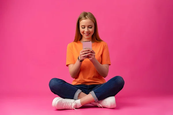 Potret seorang wanita muda menggunakan ponsel dengan latar belakang warna. Stok Gambar Bebas Royalti