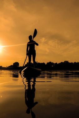 Yemek masasında bir kadın, gün batımında sörf yaparken suda yansıyor.