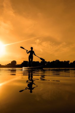 Yemek masasında bir kadın, gün batımında sörf yaparken suda yansıyor.