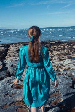 beautiful young woman posing on a rock near the sea.