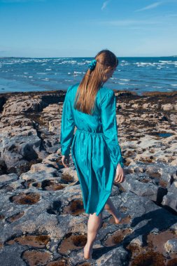 beautiful young woman posing on a rock near the sea.