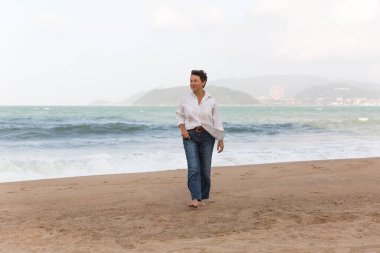 Portrait of a mature woman walking on the beach looking at the sea. Relaxed old lady strolling on the beach