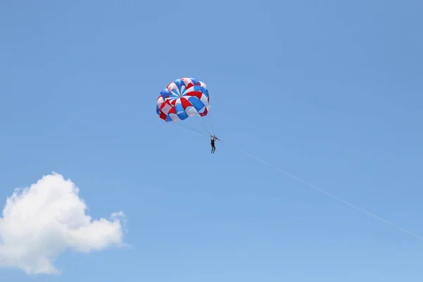 Uma mulher está deslizando usando um paraquedas no fundo do céu azul nublado. — Fotografia de Stock