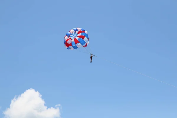 Uma mulher está deslizando usando um paraquedas no fundo do céu azul nublado. — Fotografia de Stock