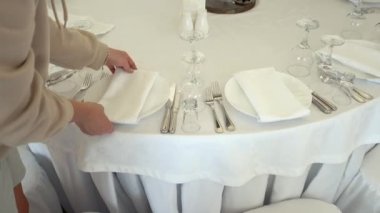 Kadınlar okyanustaki büyük bir çadırda, beyaz masa örtüleriyle kaplı büyük masalar servis ediyorlar.