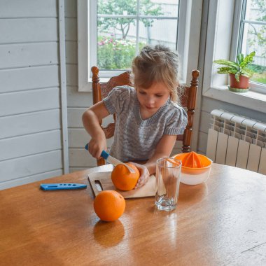 Mutfakta bir kız çocuğu portakal suyunu keser ve sıkar.