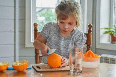 Mutfakta bir kız çocuğu portakal suyunu keser ve sıkar.