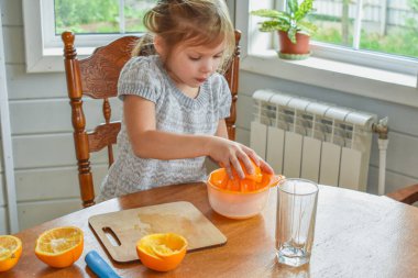 Mutfakta bir kız çocuğu portakal suyunu keser ve sıkar.