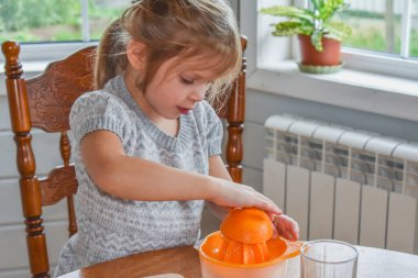 Mutfakta bir kız çocuğu portakal suyunu keser ve sıkar.