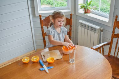 Mutfakta bir kız çocuğu portakal suyunu keser ve sıkar.