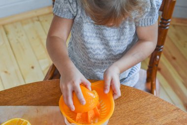 Mutfakta bir kız çocuğu portakal suyunu keser ve sıkar.