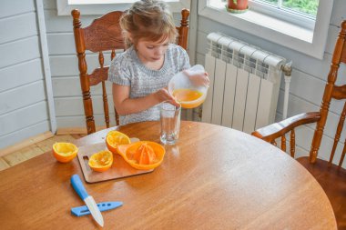 Mutfakta bir kız çocuğu portakal suyunu keser ve sıkar.