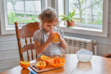 Mutfakta bir kız çocuğu portakal suyunu keser ve sıkar.