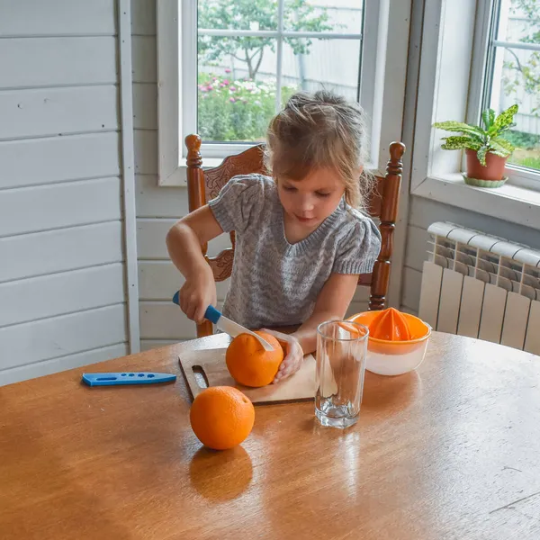 Mutfakta bir kız çocuğu portakal suyunu keser ve sıkar.
