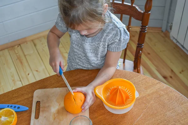 Mutfakta bir kız çocuğu portakal suyunu keser ve sıkar.