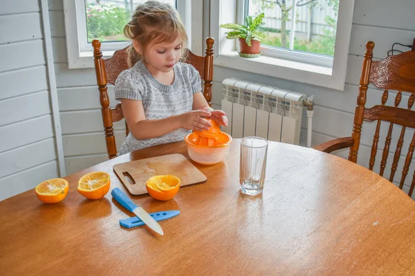 Mutfakta bir kız çocuğu portakal suyunu keser ve sıkar.