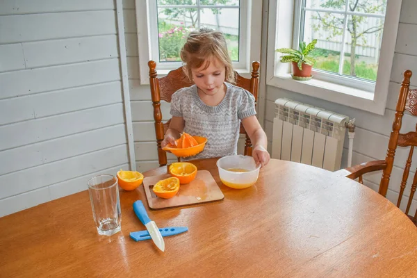 Mutfakta bir kız çocuğu portakal suyunu keser ve sıkar.