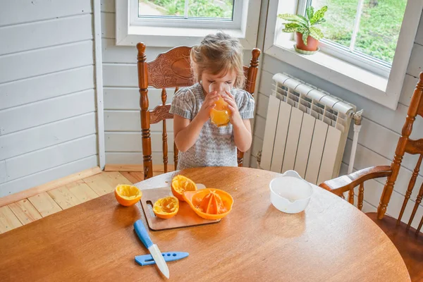 Mutfakta bir kız çocuğu portakal suyunu keser ve sıkar.