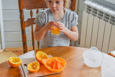 Mutfakta bir kız çocuğu portakal suyunu keser ve sıkar.