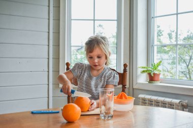 Mutfakta bir kız çocuğu portakal suyunu keser ve sıkar.