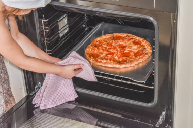 Kız çocuk fırında pizza pişiriyor. Fotoğraf filtresiz.