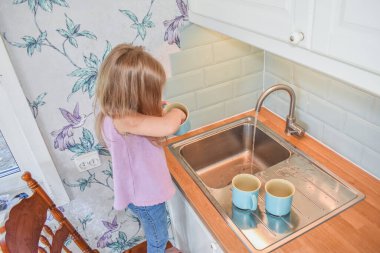 Bir çocuk lavabodaki fincanları filtresiz yıkıyor.