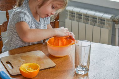 Mutfakta bir kız çocuğu portakal suyunu keser ve sıkar.