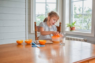 Mutfakta bir kız çocuğu portakal suyunu keser ve sıkar.