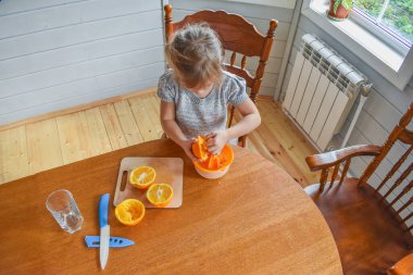 Mutfakta bir kız çocuğu portakal suyunu keser ve sıkar.