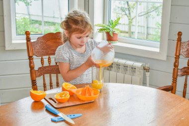 Mutfakta bir kız çocuğu portakal suyunu keser ve sıkar.