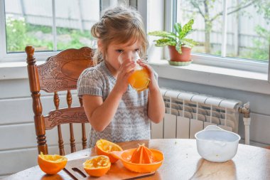 Mutfakta bir kız çocuğu portakal suyunu keser ve sıkar.
