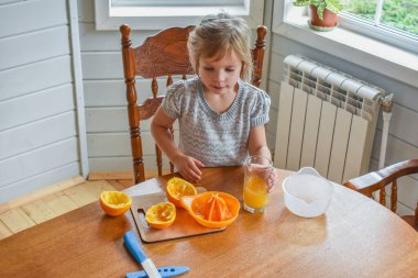 Mutfakta bir kız çocuğu portakal suyunu keser ve sıkar.