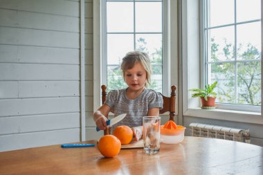 Mutfakta bir kız çocuğu portakal suyunu keser ve sıkar.