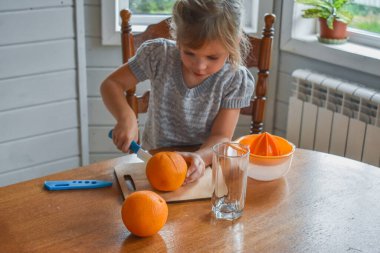 Mutfakta bir kız çocuğu portakal suyunu keser ve sıkar.