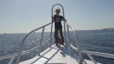 Çocuk kız bir yatın pruvasında elini açık denizde sallıyor.