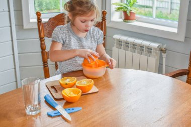 Mutfakta bir kız çocuğu portakal suyunu keser ve sıkar.