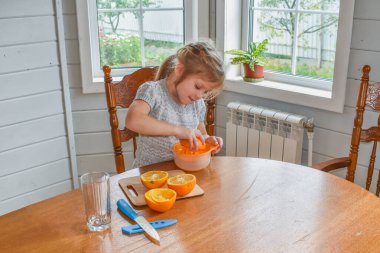 Mutfakta bir kız çocuğu portakal suyunu keser ve sıkar.