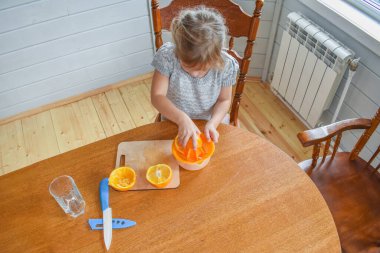 Mutfakta bir kız çocuğu portakal suyunu keser ve sıkar.