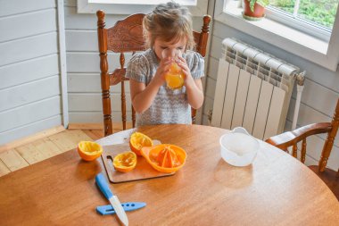 Mutfakta bir kız çocuğu portakal suyunu keser ve sıkar.