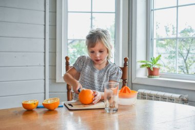 Mutfakta bir kız çocuğu portakal suyunu keser ve sıkar.