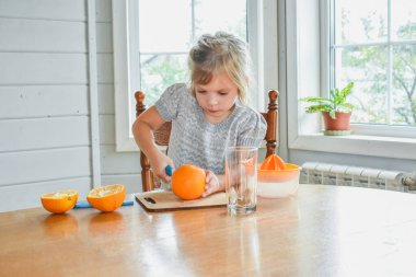Mutfakta bir kız çocuğu portakal suyunu keser ve sıkar.