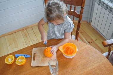 Mutfakta bir kız çocuğu portakal suyunu keser ve sıkar.