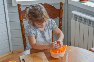Mutfakta bir kız çocuğu portakal suyunu keser ve sıkar.