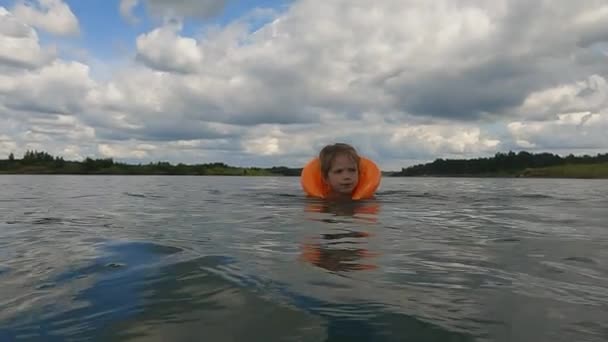 オレンジ色のインフレータブルベストの女の子が湖で泳いでいます — ストック動画